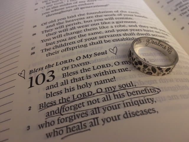 A bible opened to the book of Psalm with verses underlined, with an engraved silver ring sitting on top
