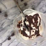 Chocolate shell recipe drizzled on top of vanilla ice cream in a glass dish on a marble surface.