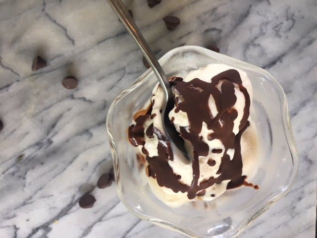 Chocolate shell recipe drizzled on top of vanilla ice cream in a glass dish on a marble surface.