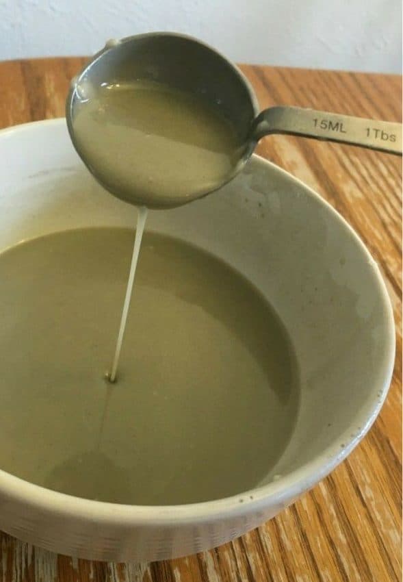 Homemade deodorant with bentonite clay in a large bowl, a spoon pouring the mixture into the bowl.