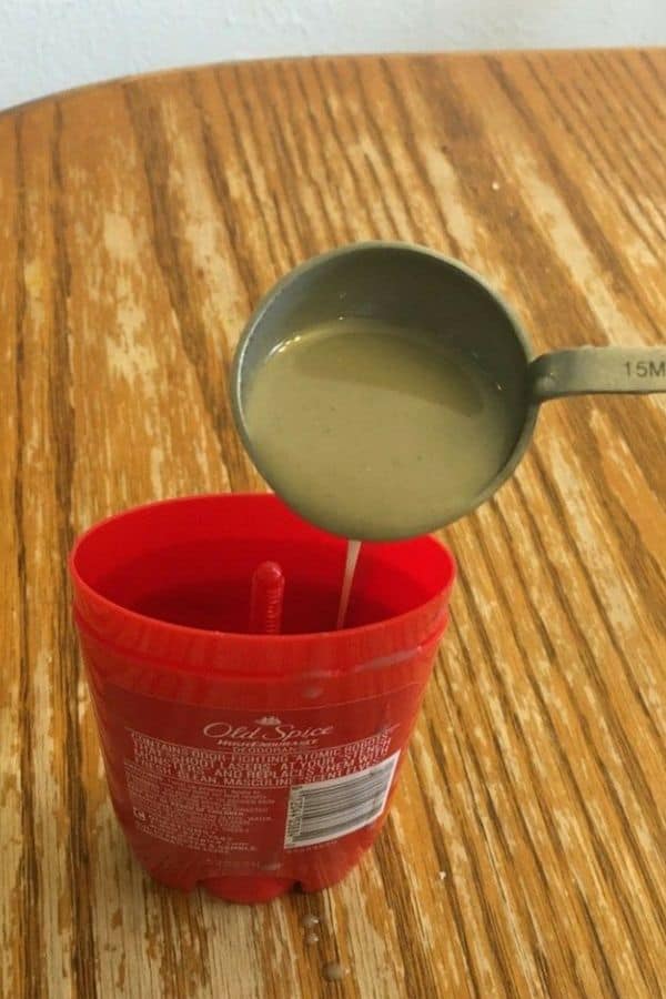 Natural deodorant being poured from a large spoon into an empty stick deodorant container.
