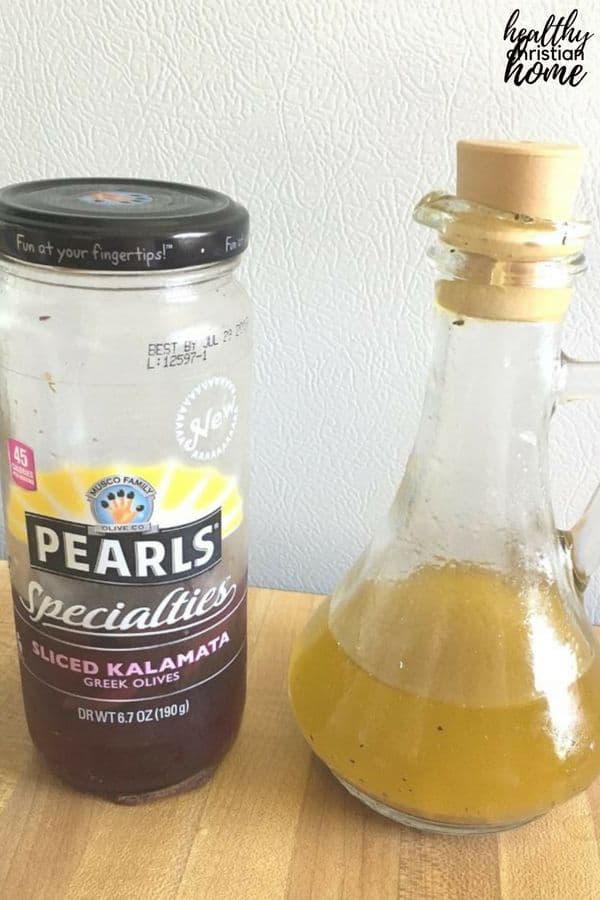 Simple greek salad dressing next to a jar of kalamata greek olives.