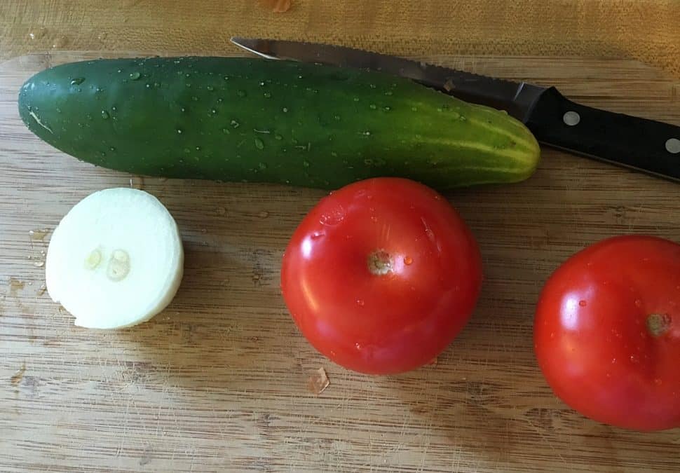 Cucumber salad prep - a large cucumber, two tomatoes, and half an onion rest on a wooden cutting board.