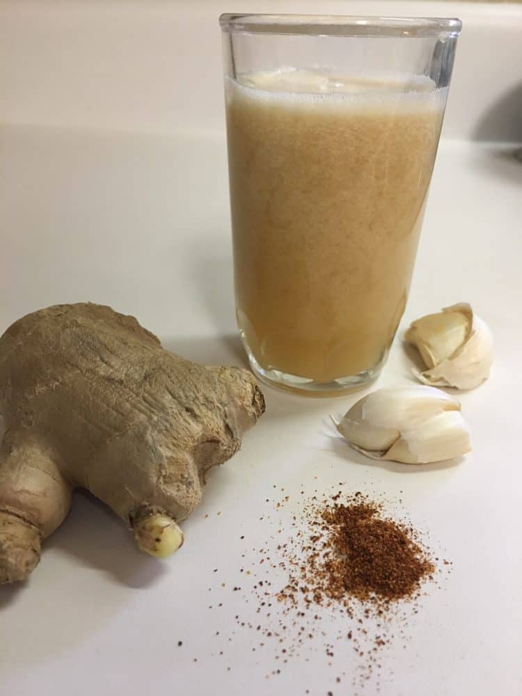 One of the best home remedies for common cold - a glass of super tonic pictured with ginger root, garlic, and cayenne pepper.