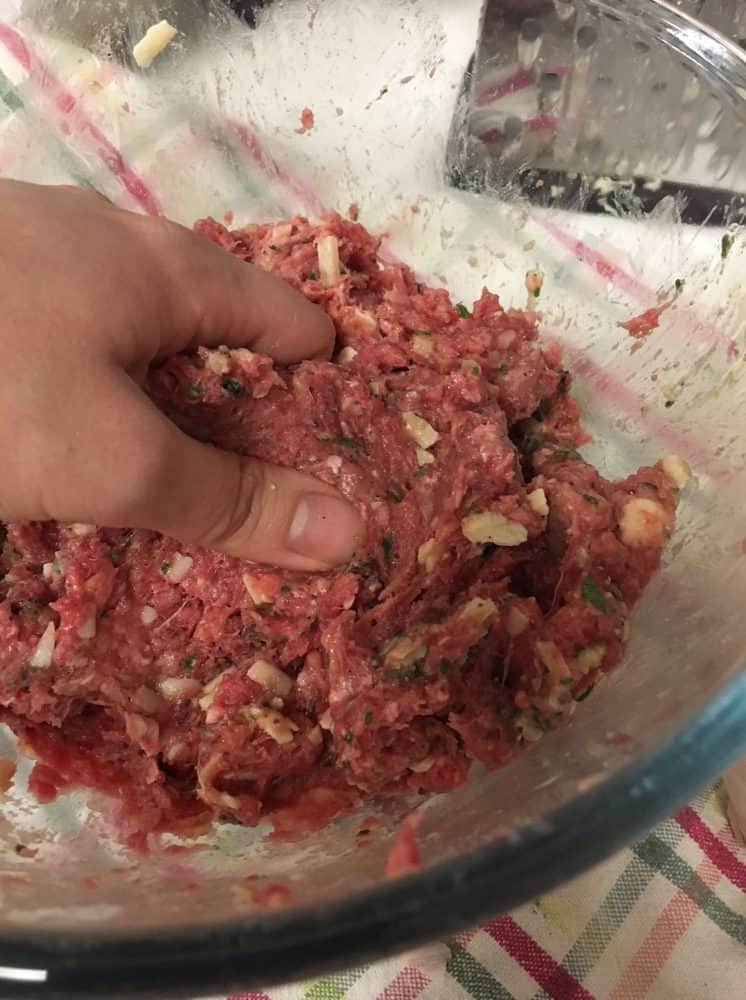 Mixing homemade meatballs by hand in a clear bowl.