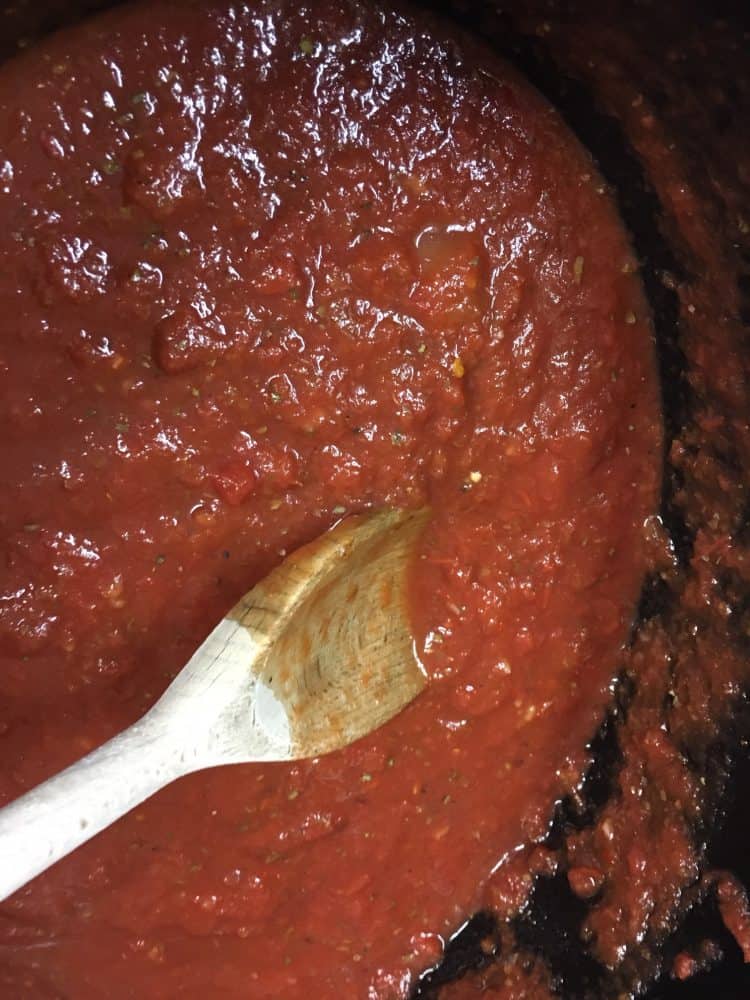 Homemade spaghetti and meatballs marinara sauce in a slow cooker with a wooden spoon.