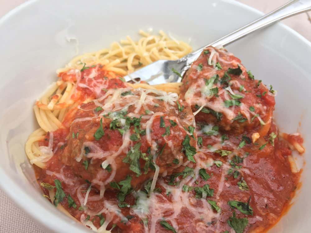 Spaghetti and meatballs with parsley in a white ceramic bowl.