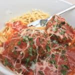 Spaghetti and meatballs with parsley in a white ceramic bowl.
