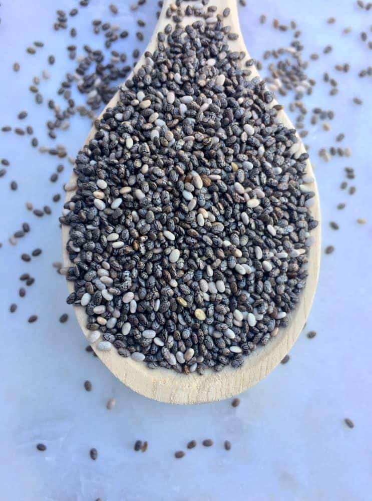Large spoonful of chia seeds with chia scattered around the spoon.