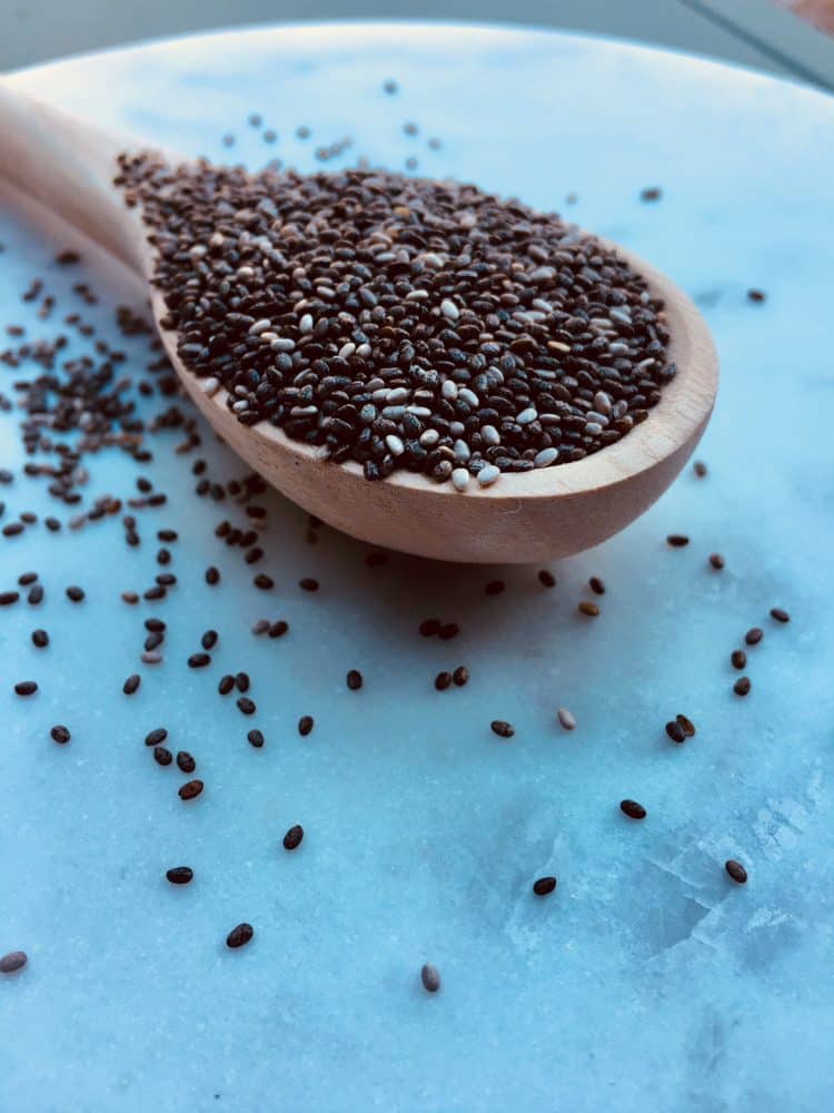 Wooden spoonful of chia seeds overflowing onto a marble board ready for chia recipes.