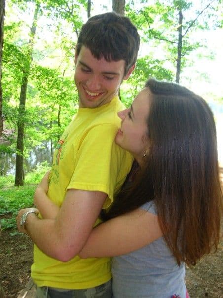 A young man and woman hugging in a green forest.