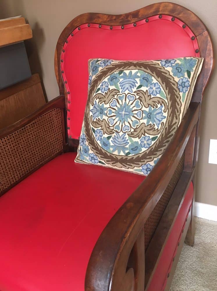 An antique red leather chair with decorative pillow.