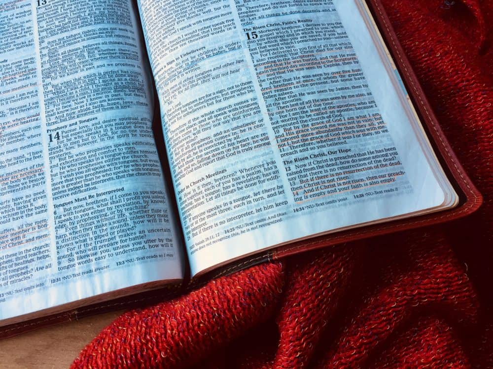 Close-up of an open bible with underlined verses next to a red blanket.