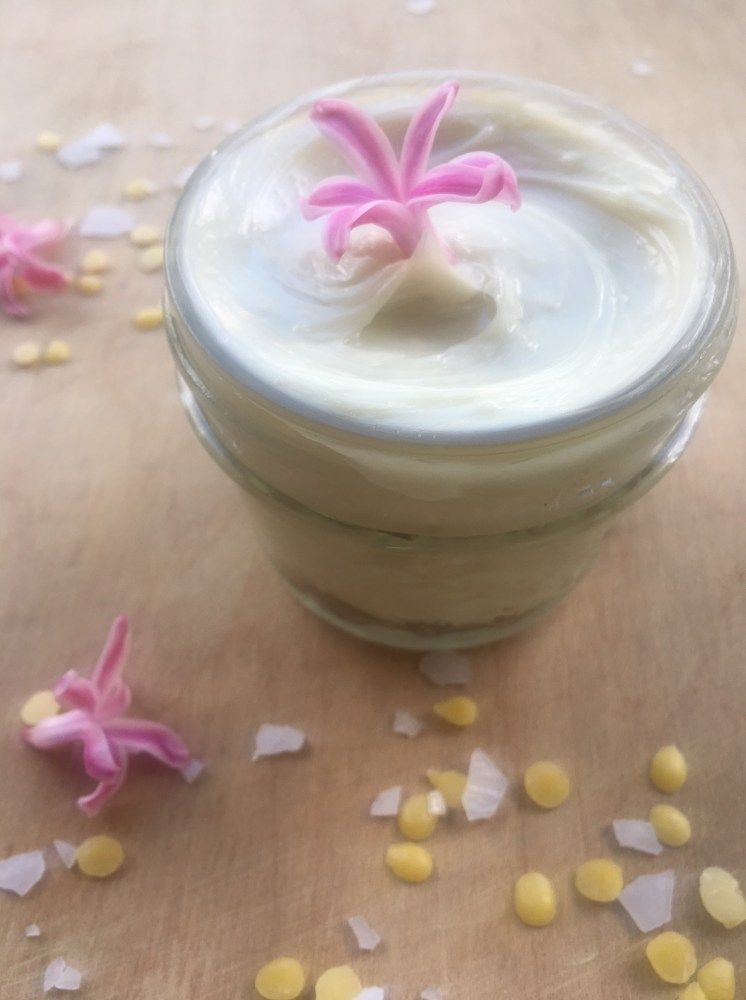 DIY magnesium lotion in a jar with pink flowers, beeswax, and magnesium flakes surrounding.