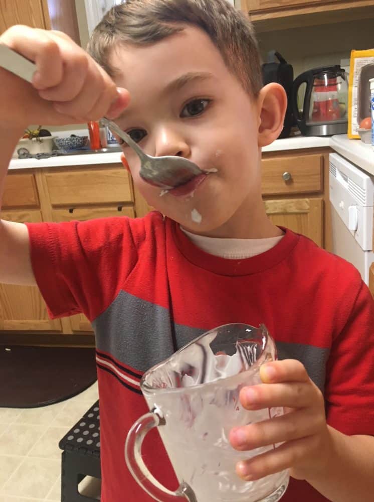 Little boy licking a spoon, helping his mom bake breakfast muffins.