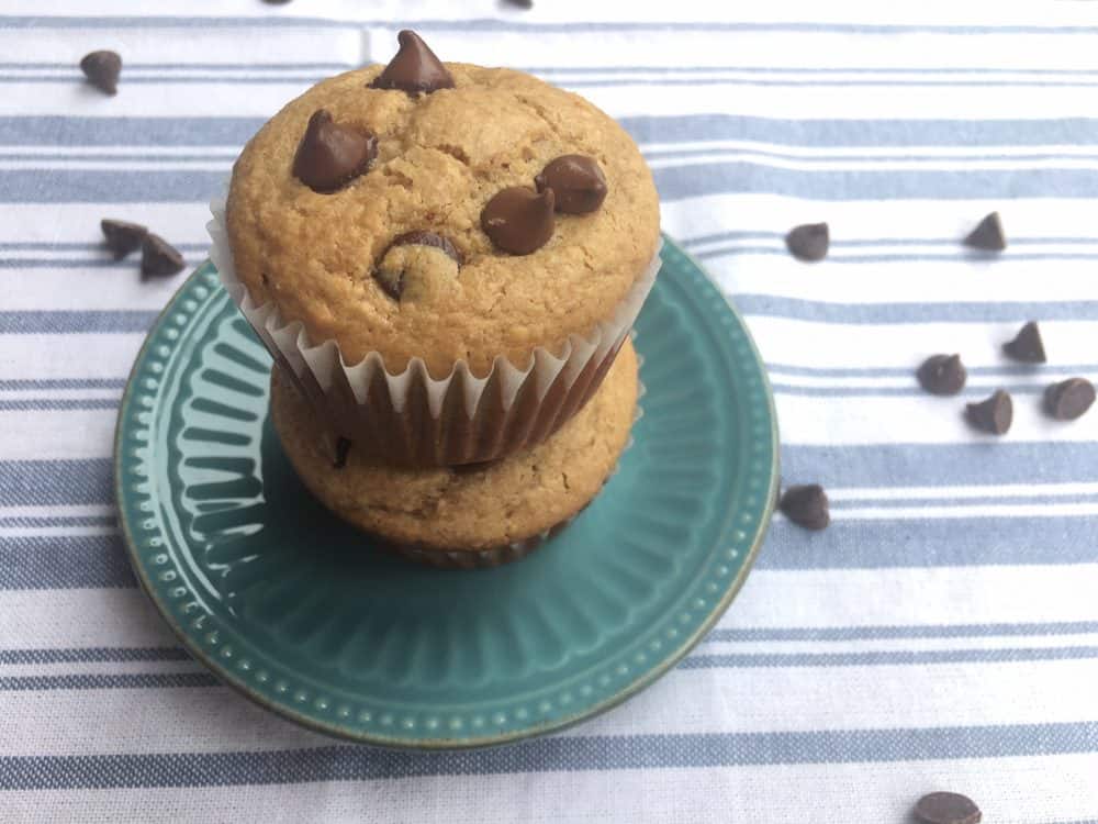 Peanut butter chocolate chip muffins, stacked on a small blue decorative plate with chocolate chips scattered around.