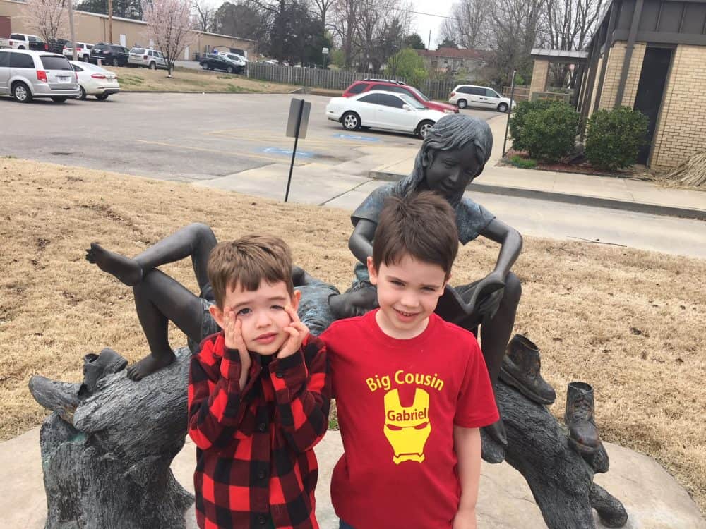 Two boys in front of a statue at the public library.