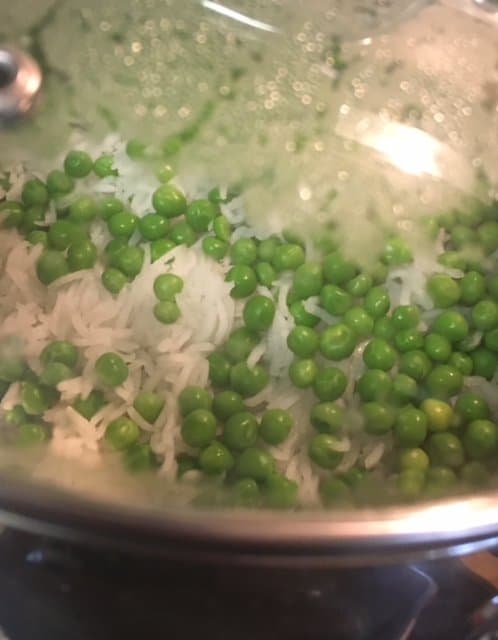 White basmati rice and bright green peas in a silver pot with a glass lid.