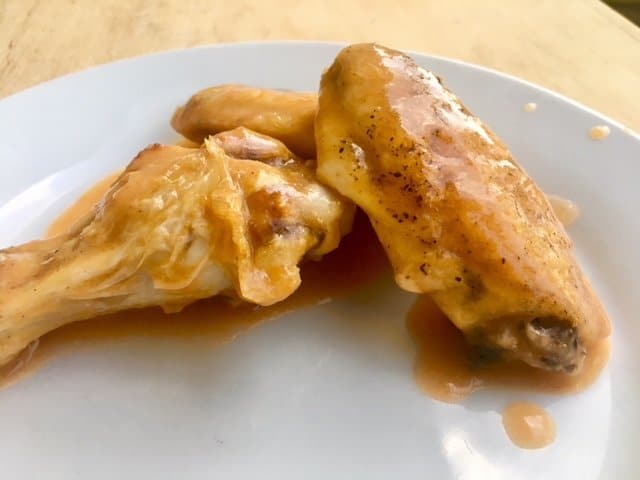 Baked chicken wings with buffalo chicken gravy on a white plate.