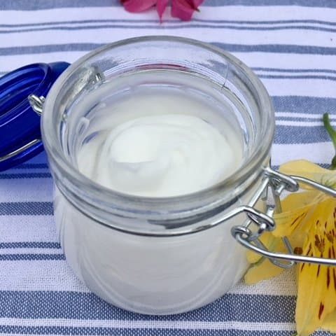 DIY body lotion in a small clear jar on a striped tea towel.