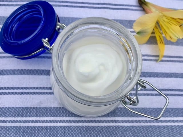 DIY lotion for natural skincare in a small jar on a striped tea towel.