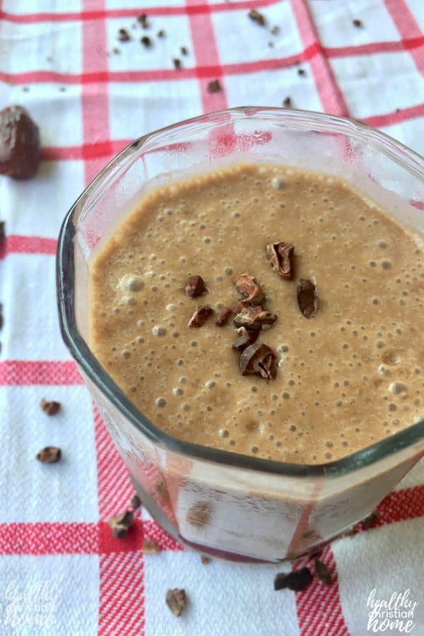 Homemade chocolate smoothie in a small glass, garnished with cacao nibs.