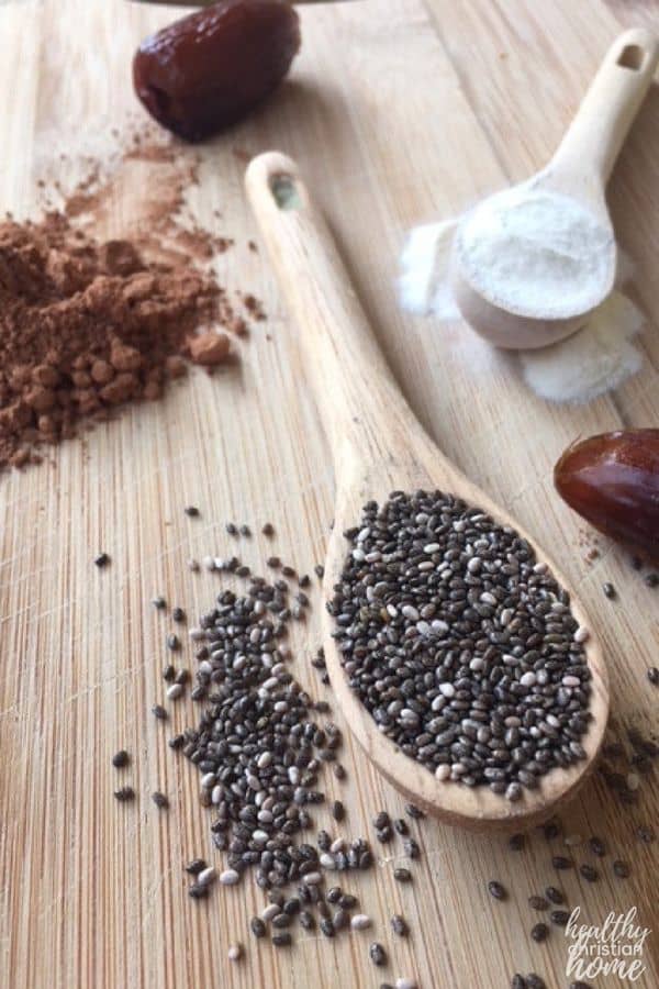 Chocolate smoothie ingredients on a wooden surface: chia seeds, cacao powder, collagen powder, dates.
