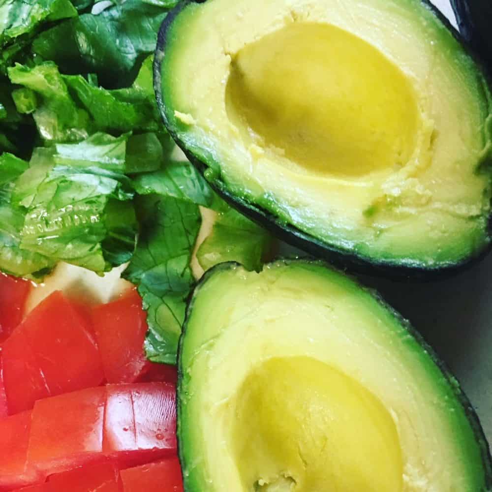 Avocado cut in half with diced tomato and lettuce on a chopping board - all part of a Bible diet.