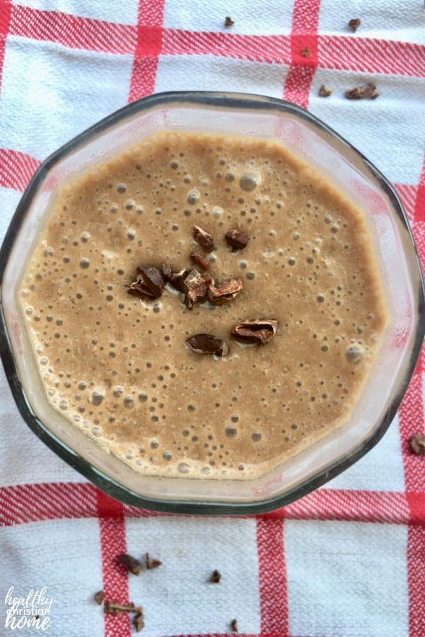 Healthy chocolate smoothie garnished with cacao nibs in a small glass on a checkered tea towel.