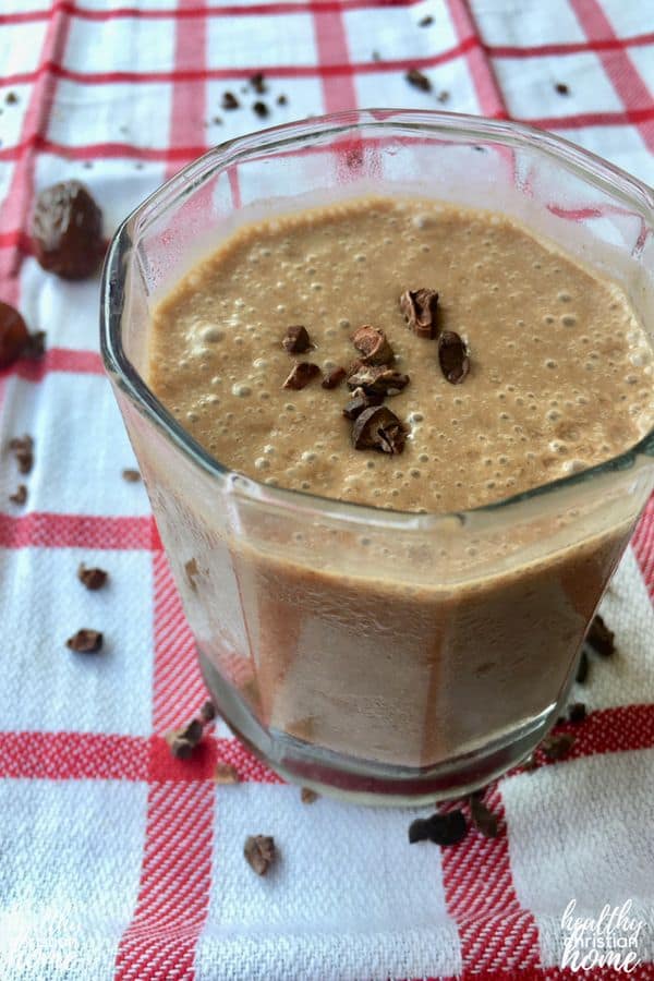 Healthy chocolate shake in a small glass cup with cacao nibs on top of a checkered tea towel.