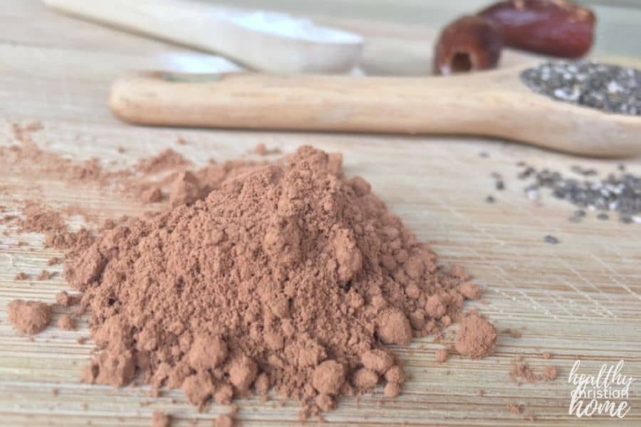 Healthy chocolate smoothie ingredients in a wooden board: cacao powder, chia seeds, collagen powder, and dates.