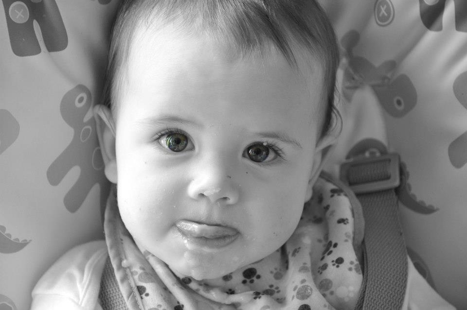 Black and white photo of a baby in a highchair licking his lips.