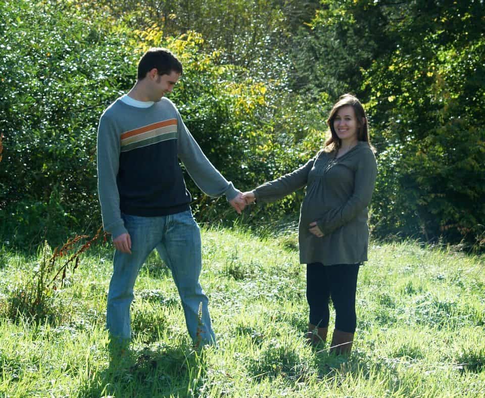 Maternity photo of man and woman holding hands in a meadow.
