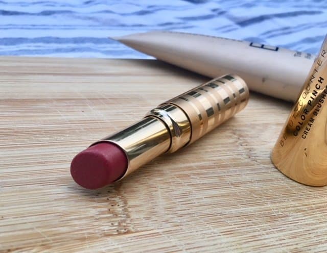 Natural makeup on a wooden surface, including lipstick in a gold tube.