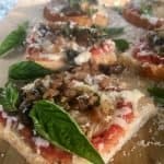 Homemade mini pizzas on a wooden board garnished with fresh basil.