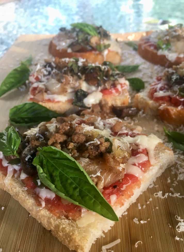 Homemade mini pizzas on a wooden board garnished with fresh basil.