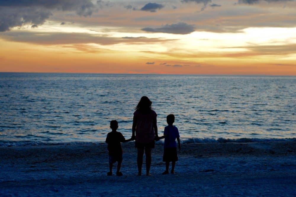 proverbs 31 woman overlooking the ocean at sunset with her two children