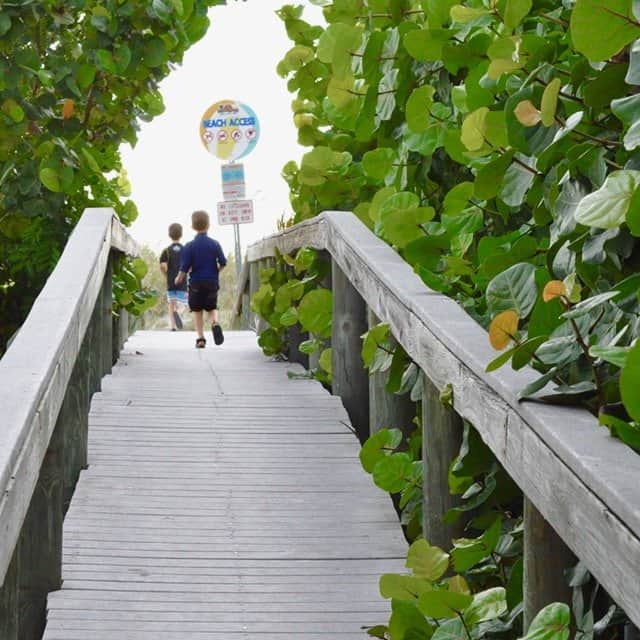 Two boys running across the boardwalk to get to the beach.