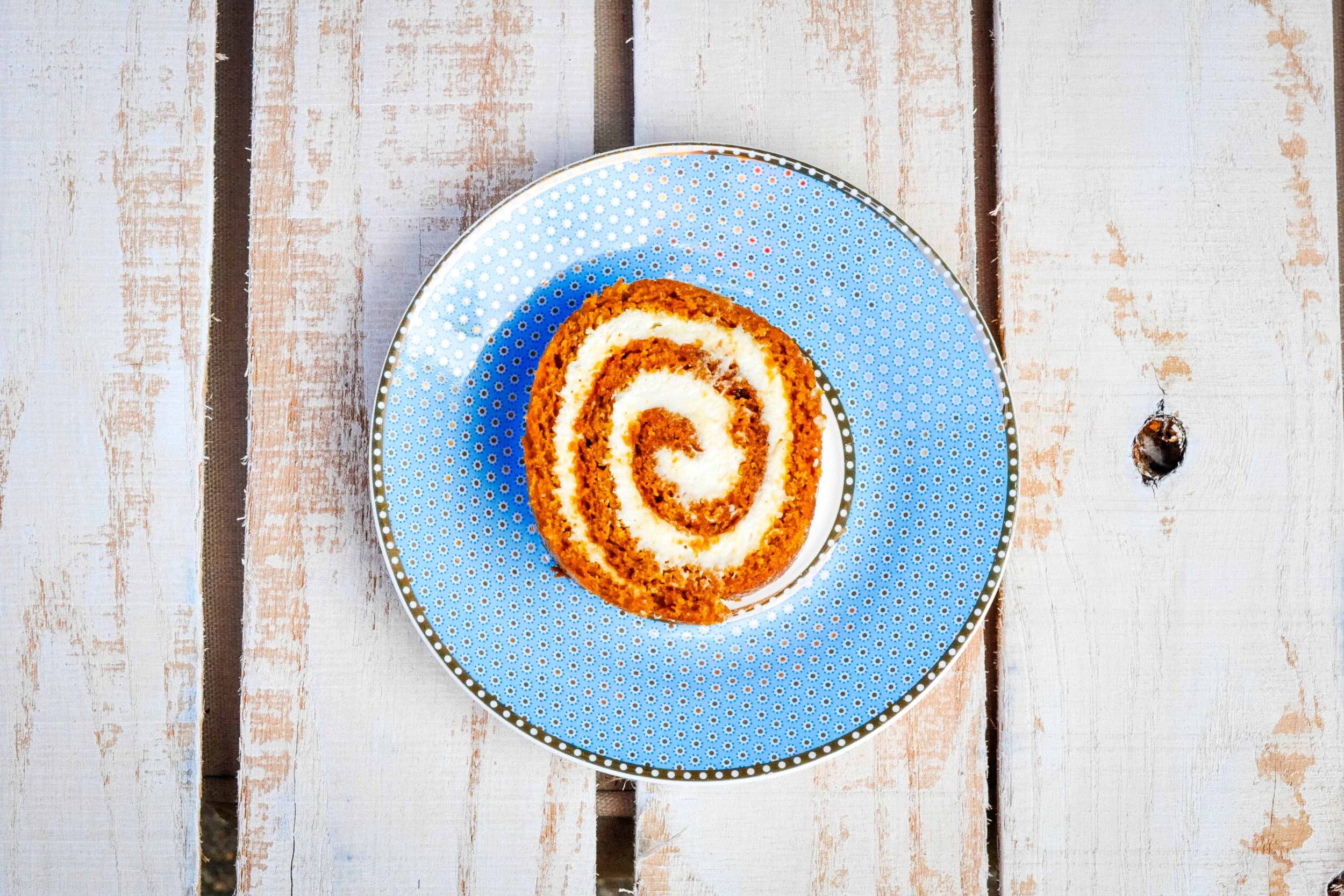 Single slice of pumpkin roll cake on a blue plate.