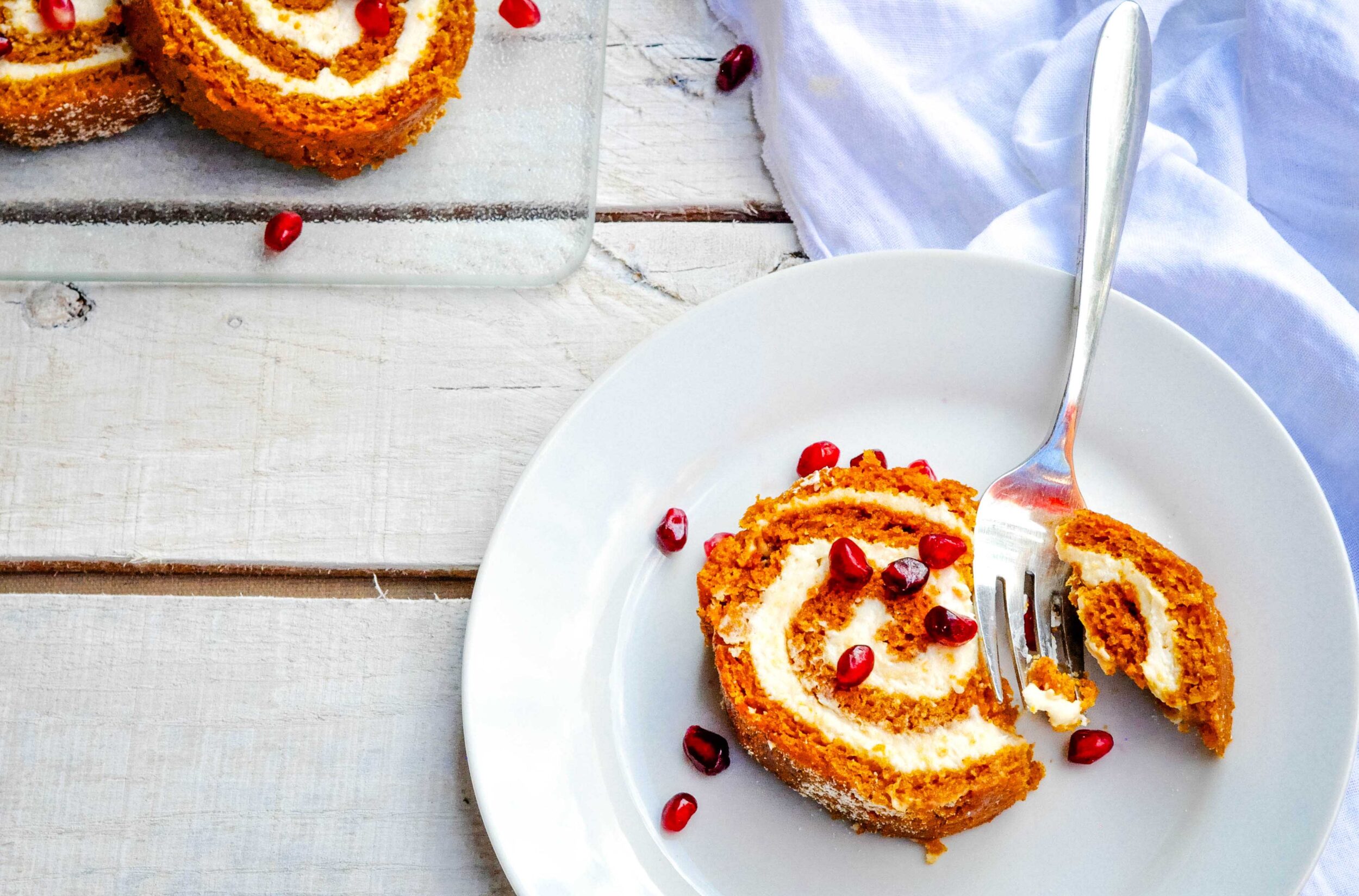 Pumpkin roll cake on a white plate with a fork and pomegranate arils.