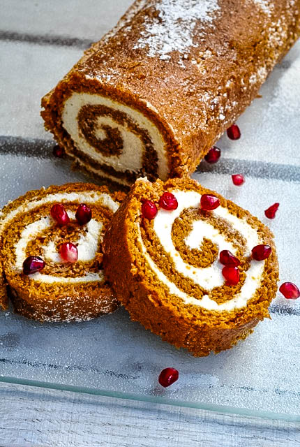 Two slices of lighter pumpkin roll with pomegranate arils sprinkled on top.