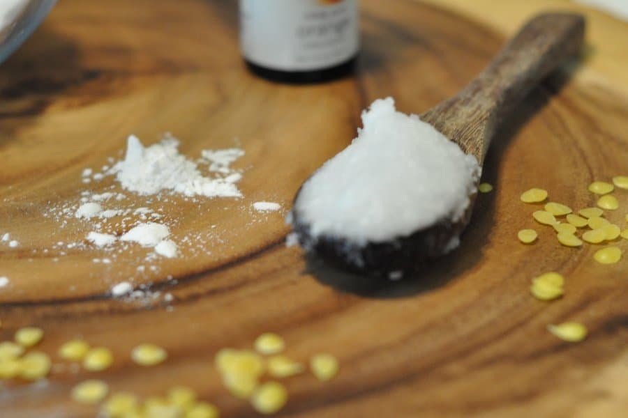 Ingredients for DIY deodorant arranged on a board: beeswax, arrowroot powder, coconut oil, and essential oil.