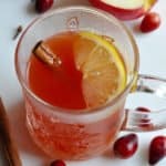 Healthy cranberry wassail in a cup garnished with cinnamon and a lemon wedge.