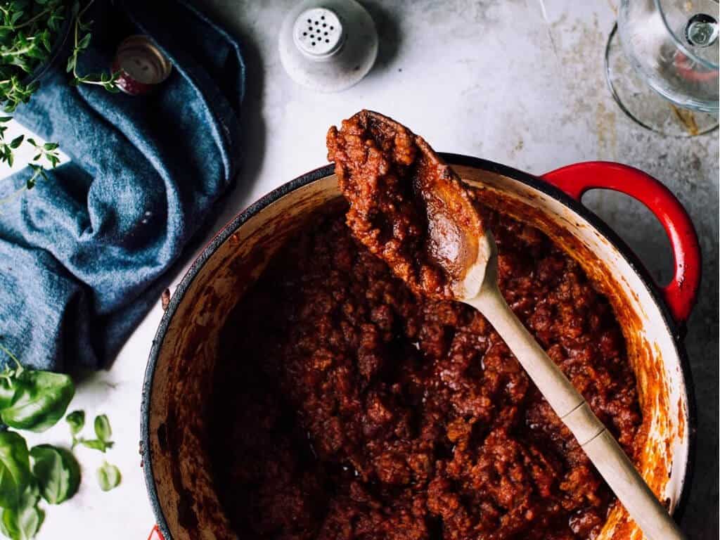 Ground beef in spaghetti sauce cooked in a red dutch oven pot.