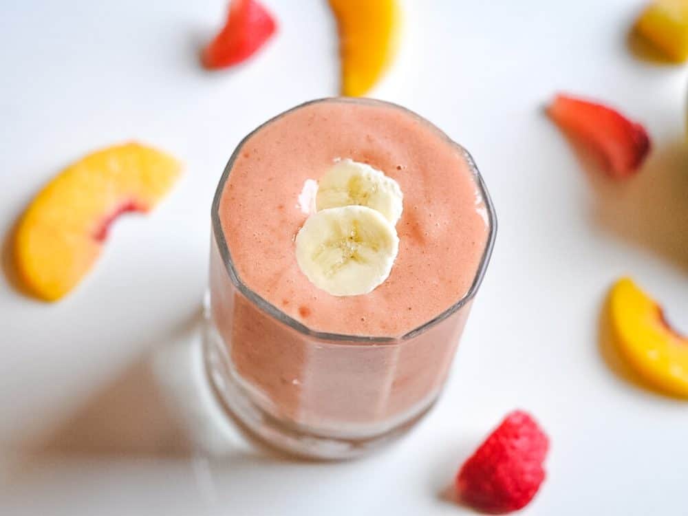 Fruit smoothie in a glass surrounded by pieces of fruit.