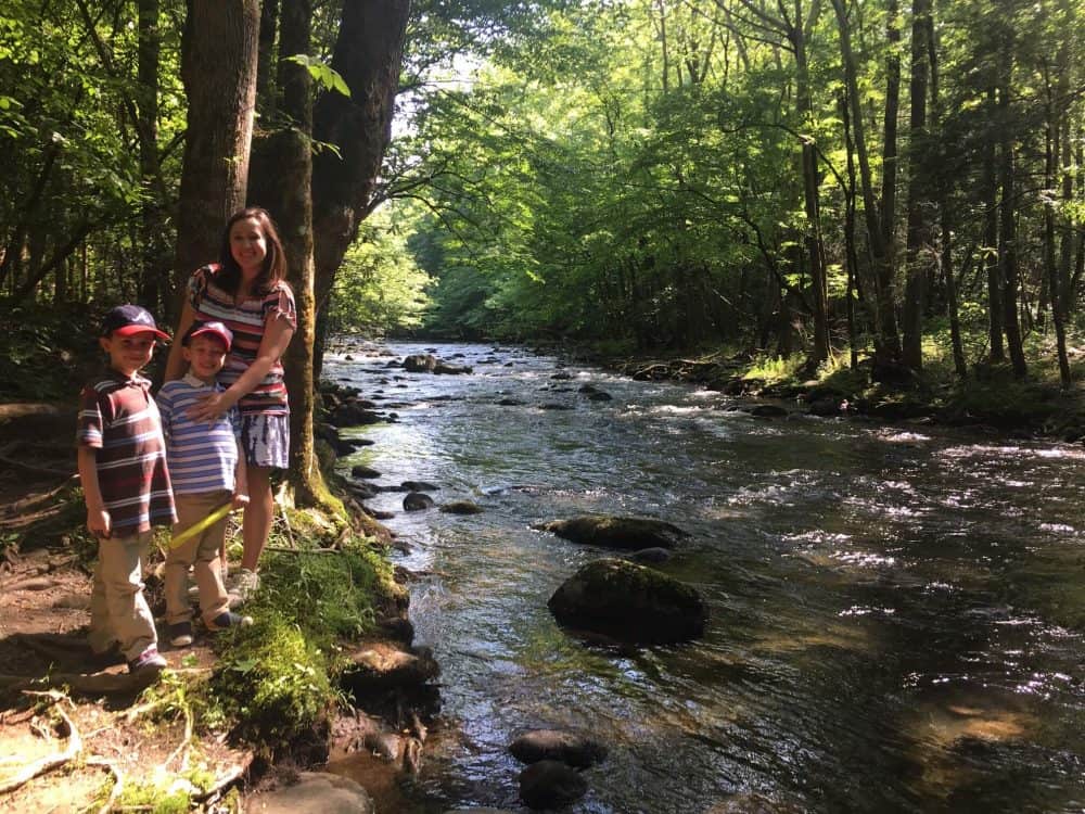 A mom and her sons hiking and exploring nature for kids next to a river.