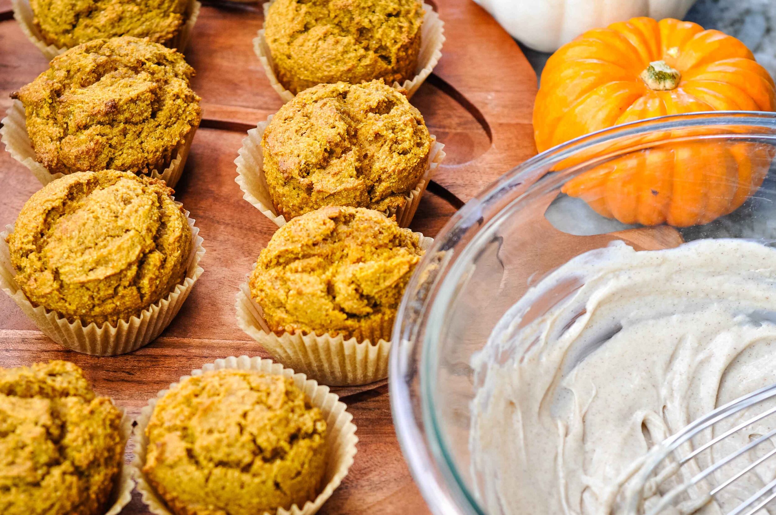 Healthy fresh milled pumpkin muffins on a platter with cream cheese honey cinnamon frosting in a bowl on the side.