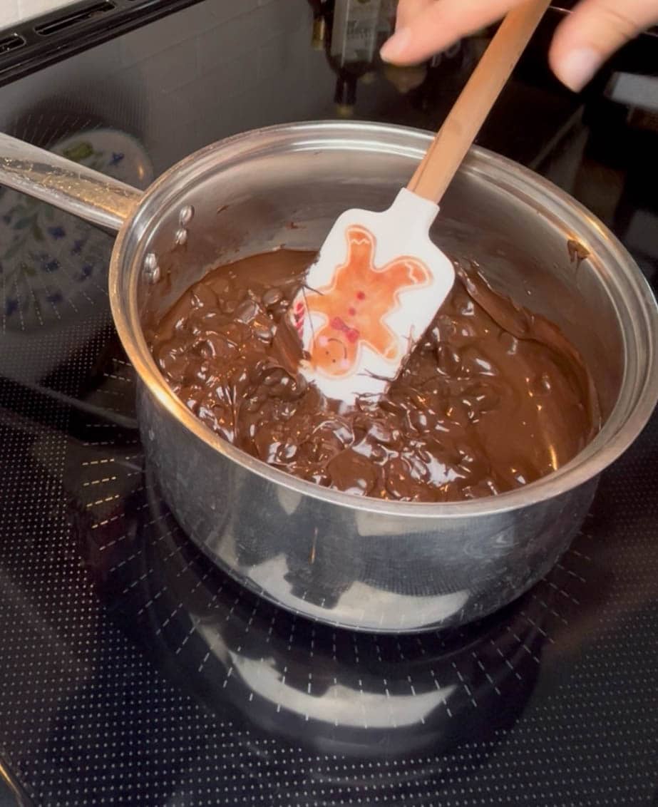 Chocolate being melted in a saucepan, stirred with a spatula.