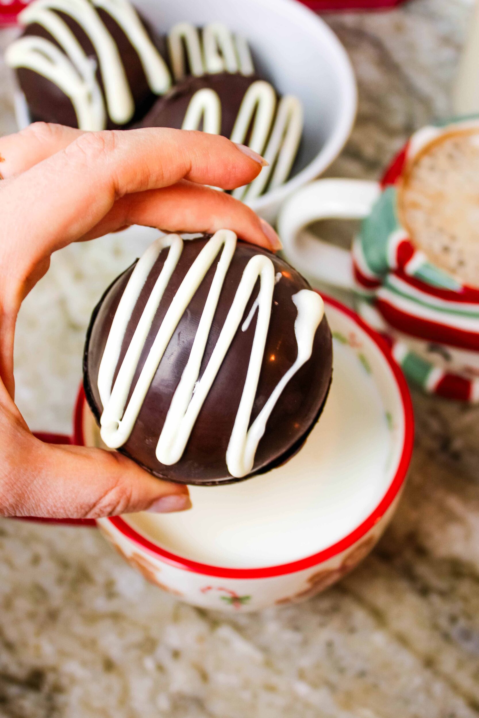 Dark chocolate cocoa bomb drizzled in white chocolate, being dropped into a mug of hot milk.