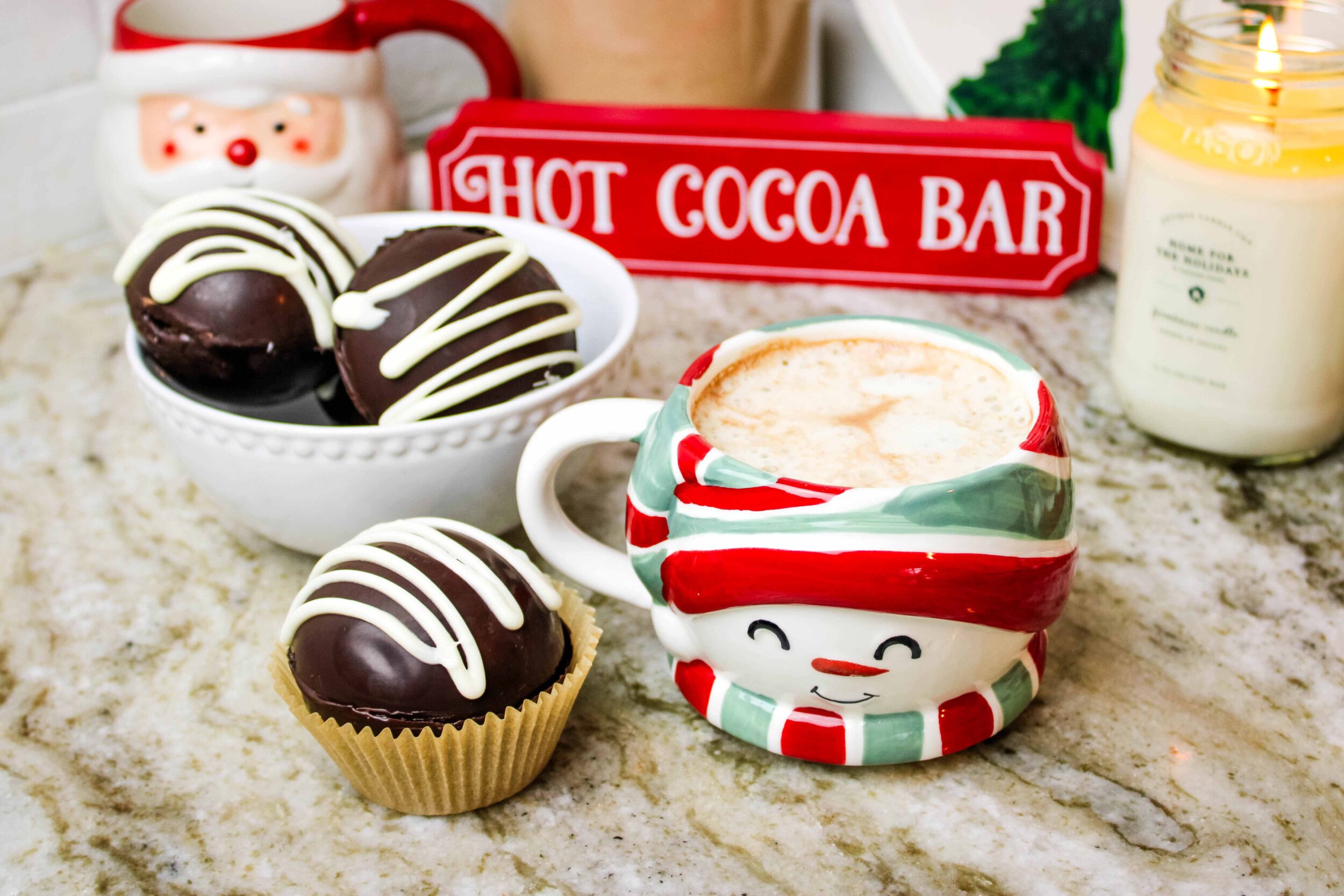 An assortment of cocoa bombs in a bowl next to a cup of hot cocoa.